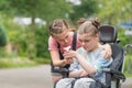 Disability a disabled child in a wheelchair relaxing outside with her sister Royalty Free Stock Photo