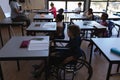 Disable schoolboy with classmates studying and sitting at desk in classroom