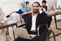 Disabled arab man in wheelchair working in office. Man is working on laptop.