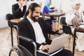 Disabled arab man in wheelchair working in office. Man is working on laptop and drinking coffee.