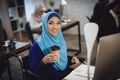 Disabled arab woman in wheelchair working in office. Woman is working on desktop computer and drinking coffee.