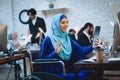 Disabled arab woman in wheelchair working in office. Woman is talking on tablet.