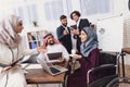 Disabled arab woman in wheelchair working in office. Woman is drinking coffe and talking to coworkers.