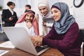 Disabled arab woman in wheelchair working in office. Woman is showing notes on laptop.