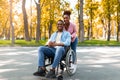 Disabled black man in wheelchair on walk with his loving wife outdoors in autumn, spending fun time together