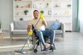 Disabled black man in wheelchair washing floor with mop at home. House cleanup concept