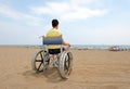 Disabled boy sitting on a wheelchair facing the sea