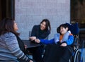 Disabled boy in wheelchair at table outdoors talking with caregivers