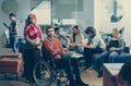 Disabled businessman in a wheelchair at work in modern open space coworking office with team