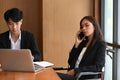 Disabled businesswoman in wheelchair talking on mobile phone while sitting with colleague. Royalty Free Stock Photo