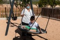 Disabled child in swing set with mother wearing a pandemic coronavirus protective mask Royalty Free Stock Photo