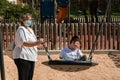 Disabled child in swing set with mother wearing a pandemic coronavirus protective mask Royalty Free Stock Photo