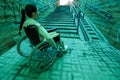 A disabled girl sitting in a wheelchair on the background of the stairs. The concept of gray everyday life of the disabled,