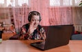 a disabled girl with slanted eyes sits at a table with headphones on and communicates while looking at a laptop