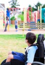 Disabled little boy in wheelchair watching children play on play Royalty Free Stock Photo