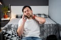 Disabled man with neck brace talking on phone with doctor, experiencing pain while sitting on couch in the living room Royalty Free Stock Photo