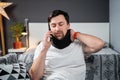 Disabled man with neck brace talking on phone with doctor, experiencing pain while sitting on couch in the living room Royalty Free Stock Photo