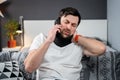 Disabled man with neck brace talking on phone with doctor, experiencing pain while sitting on couch in the living room Royalty Free Stock Photo