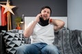 Disabled man with neck brace talking on phone with doctor, experiencing pain while sitting on couch in the living room Royalty Free Stock Photo