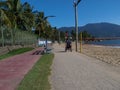 A disabled man in a wheelchair approaching the viewer. He is using the pedestrian pathway on the island of Ilhabela, Brazil, which