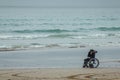 Disabled man in the wheelchair at the beach looking at mobile phone.