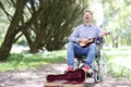 Disabled man in wheelchair plays guitar in park and makes money Royalty Free Stock Photo