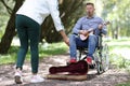 Disabled man in wheelchair plays guitar in park passers-by give money. Royalty Free Stock Photo