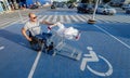 Disabled man in wheelchair pushing cart in front of himself at supermarket parking Royalty Free Stock Photo