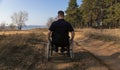 A disabled man in a wheelchair rides heavily on a sandy road along the forest Royalty Free Stock Photo