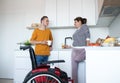 Disabled mature woman in wheelchair talking to friend in kitchen indoors at home. Royalty Free Stock Photo