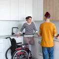 Disabled mature woman in wheelchair talking to son in kitchen indoors at home. Royalty Free Stock Photo