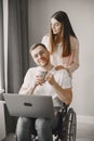 Young man in wheelchair using laptop and girlfriend hugging him at home