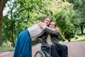 Disabled people, palliative care. Lifestyle summer portrait of senior bearded man in wheelchair hugging his young pretty Royalty Free Stock Photo