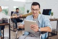 Disabled person in the wheelchair works in the office. In his hands is a tablet.