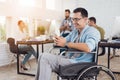 Disabled person in the wheelchair works in the office. He talks on smartphone.