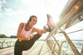 Disabled positive woman in sportswear and headphones stretching prosthetic leg while standing on the bridge. Listening Royalty Free Stock Photo