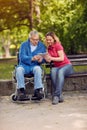 Disabled retiree man in park using tablet with daughter