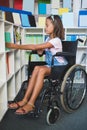 Disabled school girl selecting a book from bookshelf in library Royalty Free Stock Photo