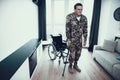 Disabled Soldier Leans on Crutch near Wheelchair