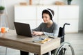 Disabled teen boy listening to music while doing online homework on laptop, indoors Royalty Free Stock Photo