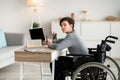 Disabled teen boy in wheelchair studying online with textbooks and laptop at home, mockup for design on pc screen Royalty Free Stock Photo