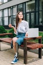 Disabled woman with apple sitting on bench and using laptop on street