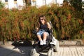 Disabled woman with reduced mobility and small stature in an electric wheelchair posing happily in the street on a sunny day.