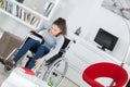 Disabled woman trying to get book wheelchair in living room Royalty Free Stock Photo