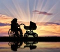 Disabled woman in wheelchair and pram reflection in water sunset