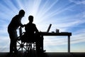 Disabled work. Silhouette worker supports and helps a disabled man