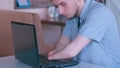 Disabled young man with amputated two stump hands in cafe works types on laptop.