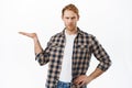 Disappointed adult man with red hair, holding an object in open hand, looking judgemental, showing an item in his palm