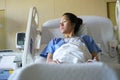 Disappointed Asian chinese woman patient lying in hospital ward and looking out of the window