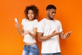 Disappointed black millennial man and woman looking at smartphones